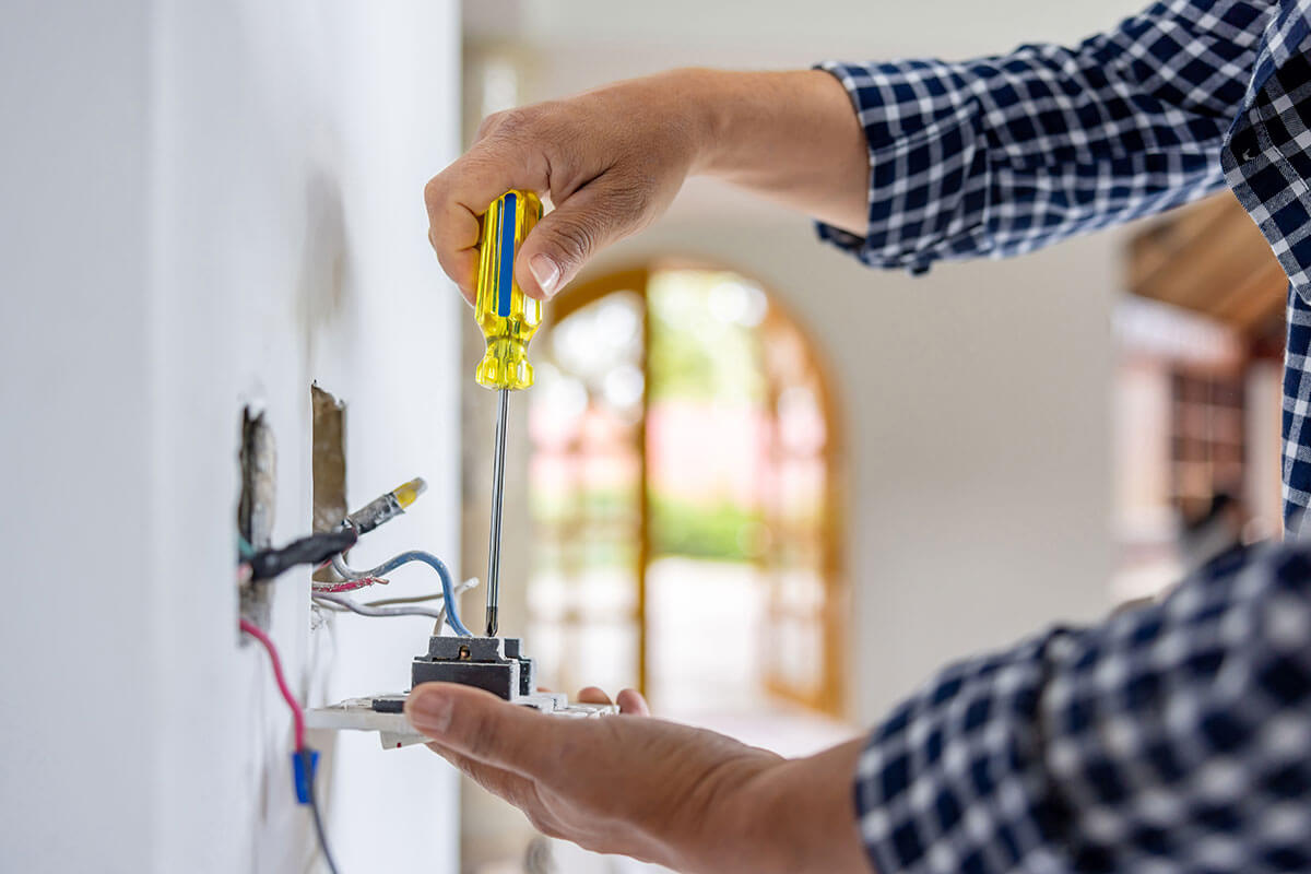 electrician installing electrical outlet in home with screwdriver