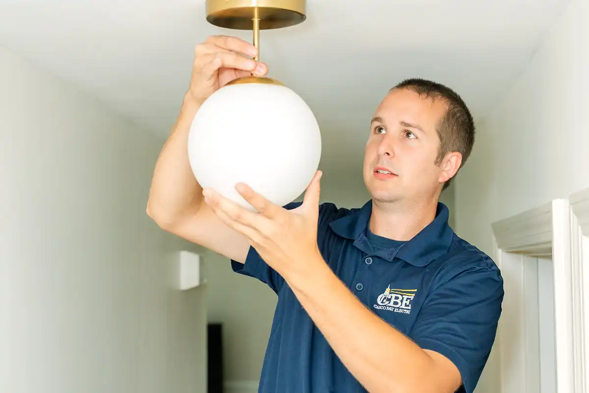 CBE electrician installing light fixture to ceiling